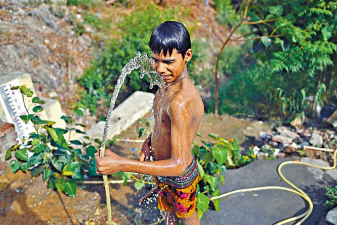 新德里一名小童在酷热天气下，以水喉淋身。