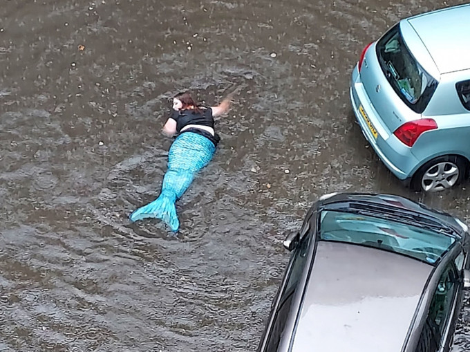一名女子披散著頭髮，穿上水藍色美人魚套裝在馬路上的積水內游動。網圖
