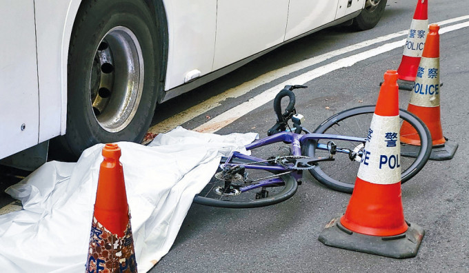 女死者倒卧旅游巴右后轮旁边，警员用白布遮盖遗体。