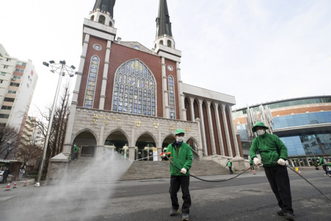 韩国首尔的Myungsung教堂前，戴著口罩的工人喷洒消毒剂以预防新冠状病毒。AP