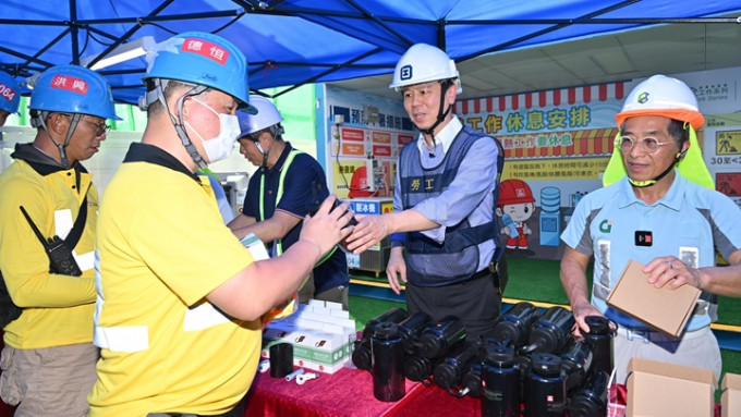 署理勞工處處長馮浩賢（右二）和建造業議會主席何安誠（右一）向工友派發消暑用品。　政府新聞處圖片