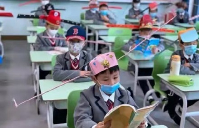 杭州一間小學復課小學生頭戴「一米帽」防疫，上課弄得像「百官上朝」。（網圖）