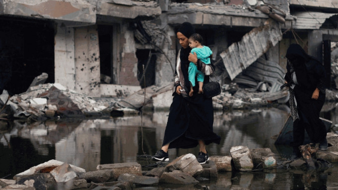 一名妇女抱着孩子在被毁的建筑物旁。（路透社）