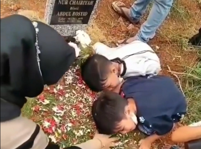 两人将耳朵贴在坟上等待亡母的「回应」。影片截图