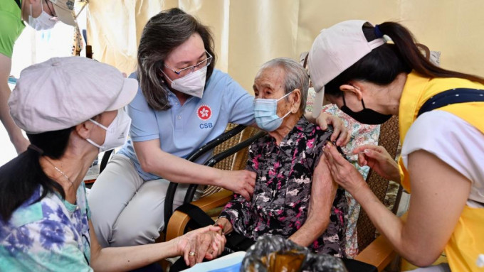 杨何蓓茵（右三）在大澳陪伴百岁长者（右二）打疫苗。政府图片