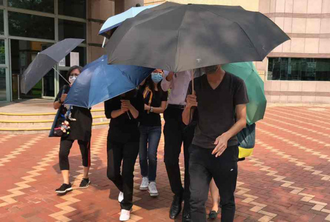 被告罗晓锋(白恤衫者)月前上庭后在伞阵保护下离开法院。资料图片