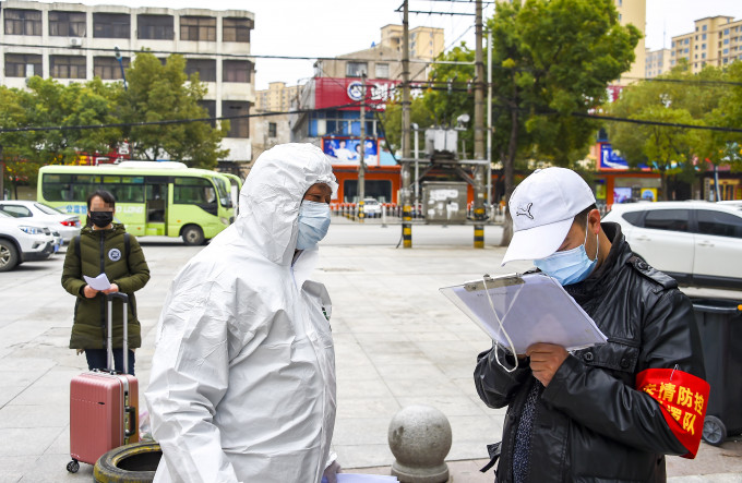 在孝感市城区一处「康复驿站」隔离点，志愿者和工作人员在交接，一名出院患者在身后等待。新华社