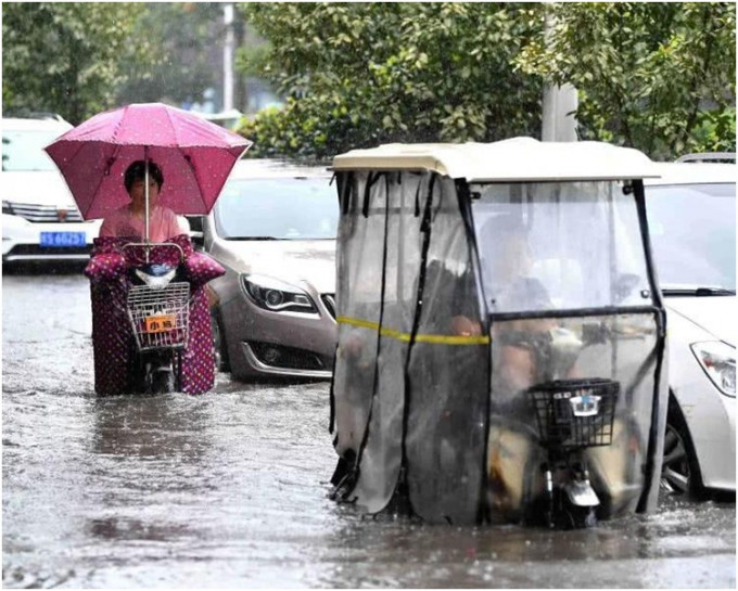 市民在街头积水路段骑车冒雨出行。网图