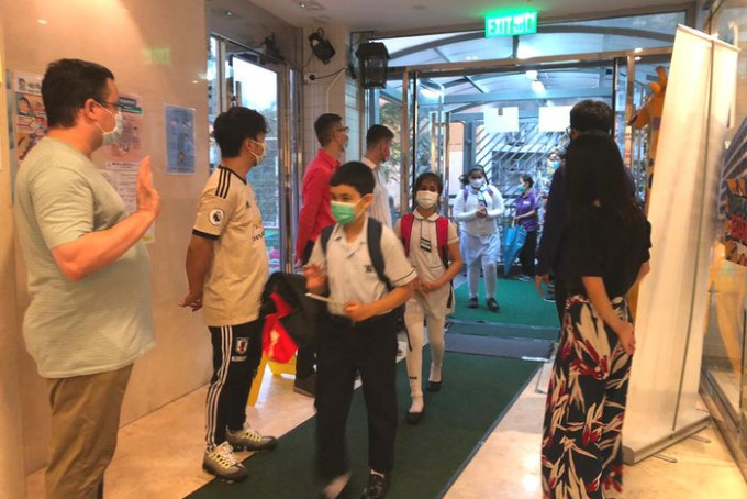 有學校教師在校門處走廊列隊歡迎學生返校，與學生打招呼。