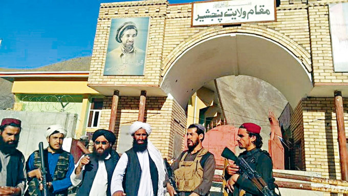 塔利班分子周一在潘杰希尔省省长官邸大门外拍照，大楼上方已故反抗军领袖马苏德的肖像，其后遭塔利班破坏。
