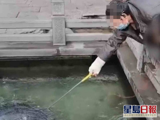 老翁用自製工具「吸」取泉池硬幣。網圖