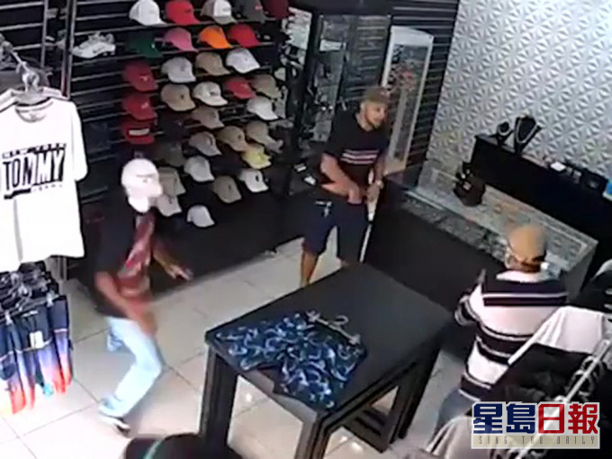 店老闆(褐色衫戴帽者)從櫃檯後步出及掏槍擊退劫匪。(網圖)