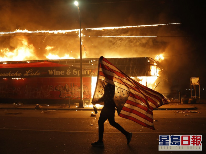 男子舉起倒轉了的美國國旗在火光中獨自向前走。AP