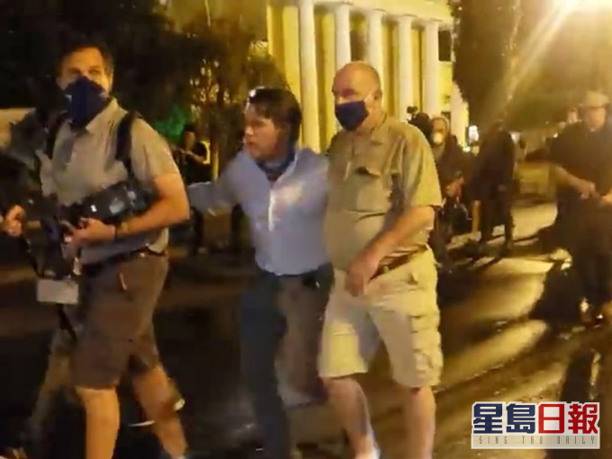 维泰特与摄影师在两名保安人员护送下离开现场。网图